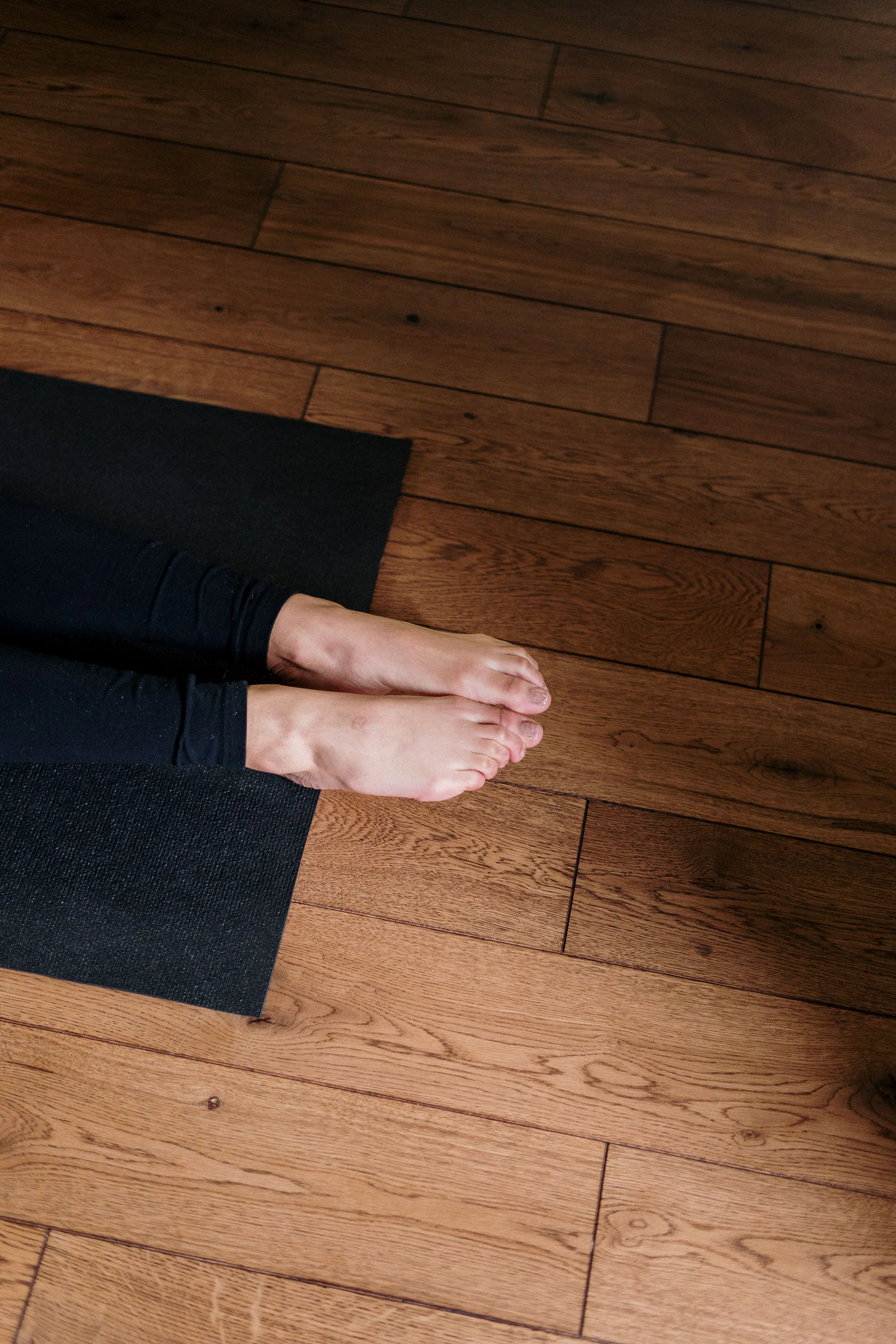 Blote voeten op een zwarte yogamat op een houten vloer.